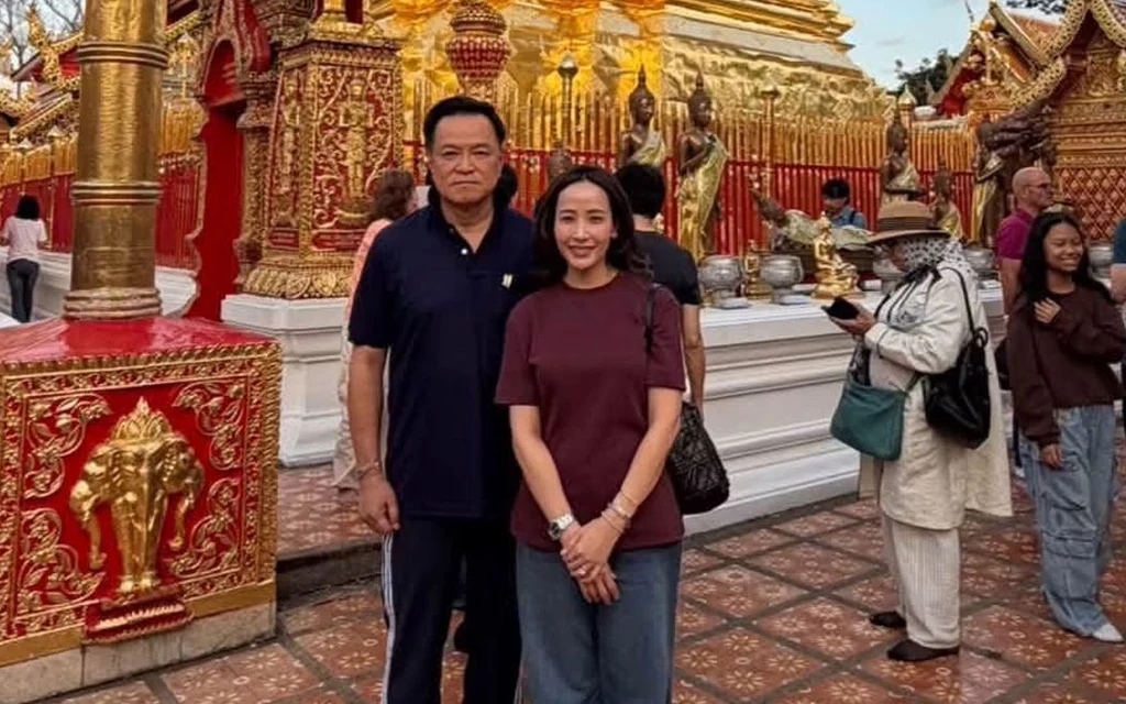 A man and woman pose at an ornate Thai temple with visitors nearby.