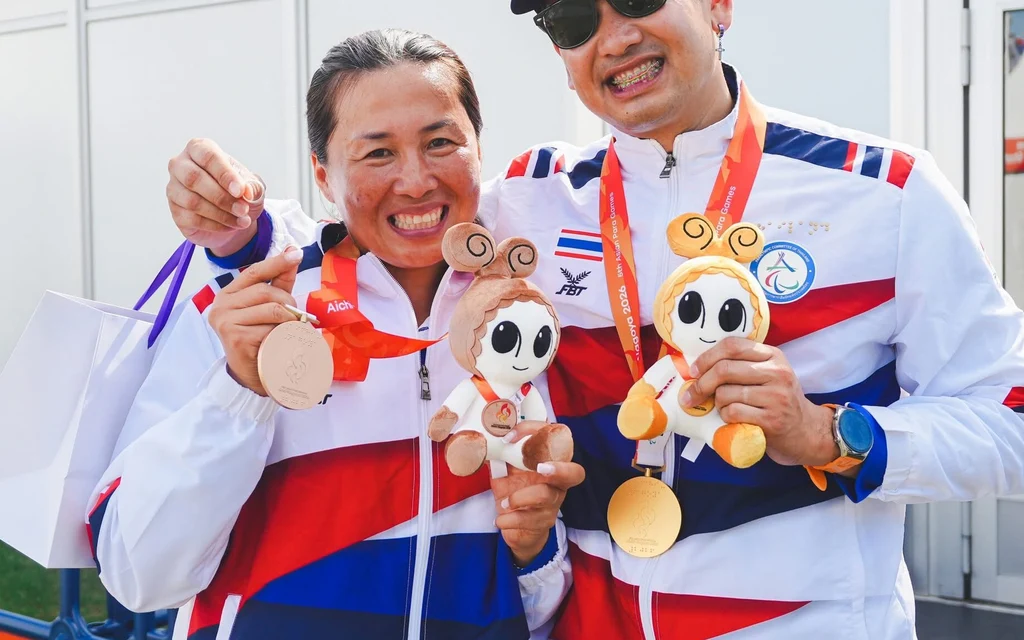 Two Thai archers pose with medals and mascot dolls.