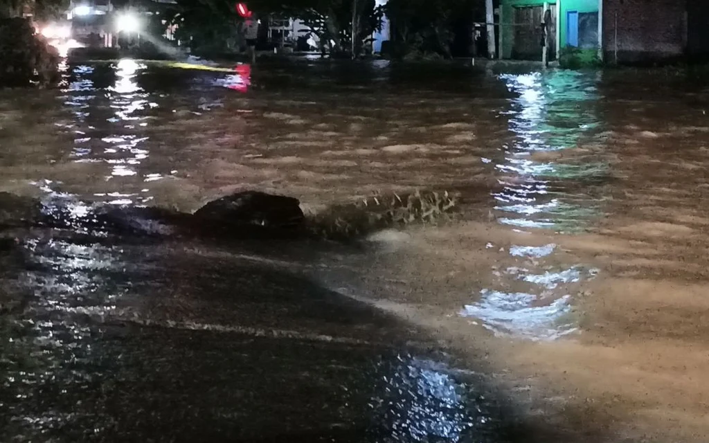 Nighttime flash flooding inundates a street beside homes.