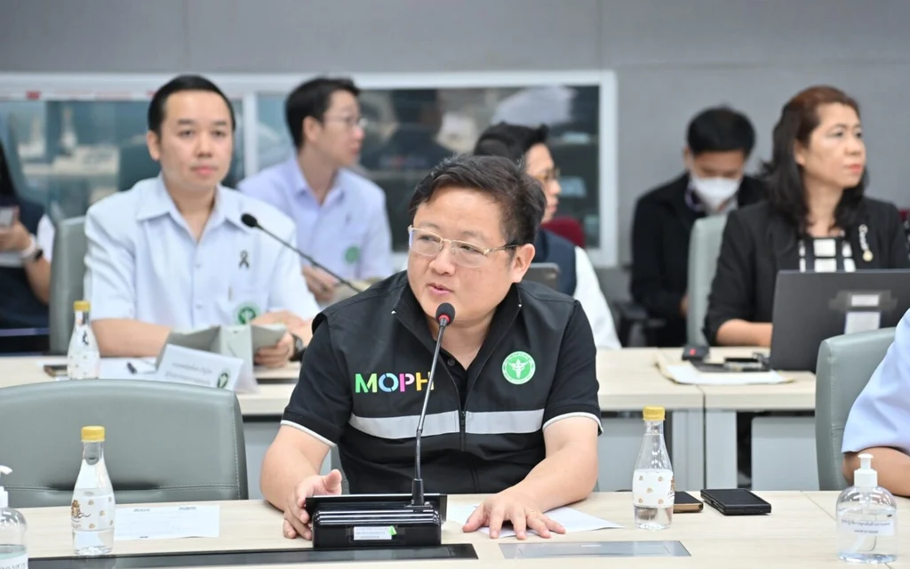 A man speaking at a meeting with other attendees in background.