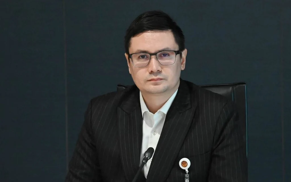 Man in a dark suit seated at a conference table
