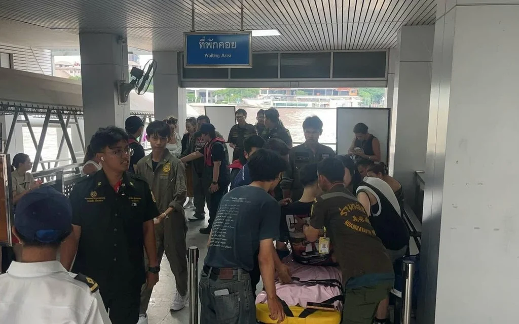People assist an injured person on a stretcher at a pier waiting area.