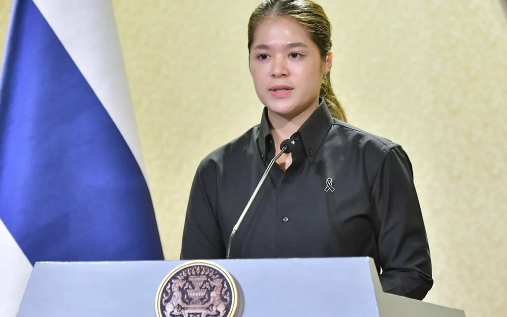 Woman speaks at a podium beside the Thai flag.