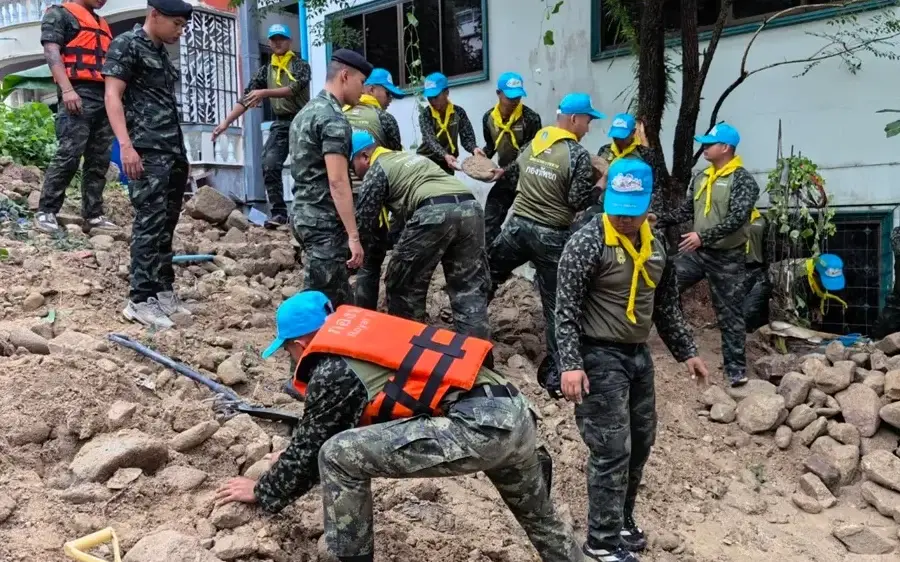 Rescue workers clear mud and rocks beside a building after a landslide.