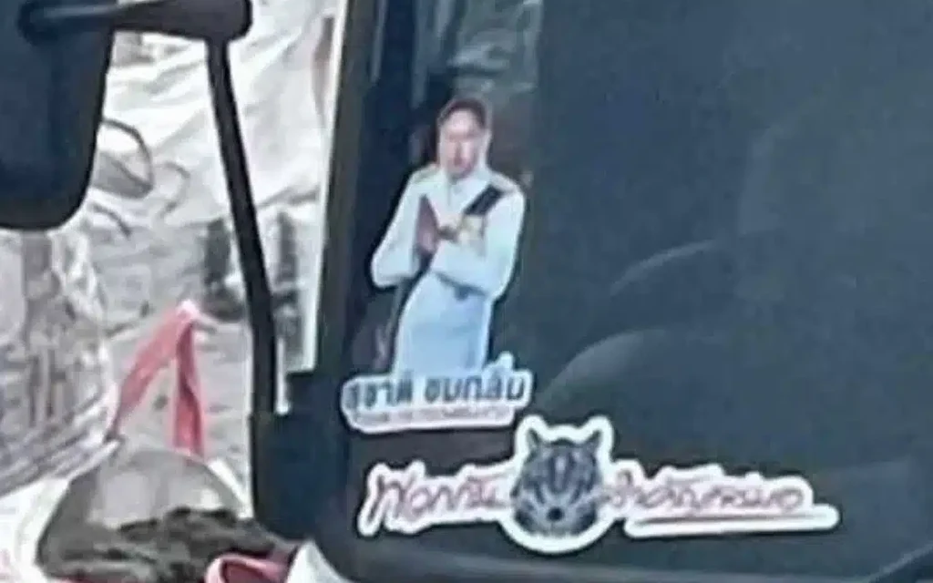 A vehicle window displays stickers, including a politician's portrait and Thai text.