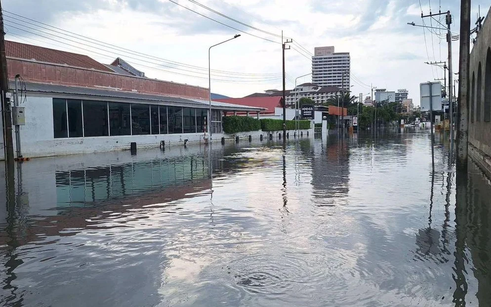 A flooded Pattaya street reflecting buildings, utility poles, and a cloudy sky.