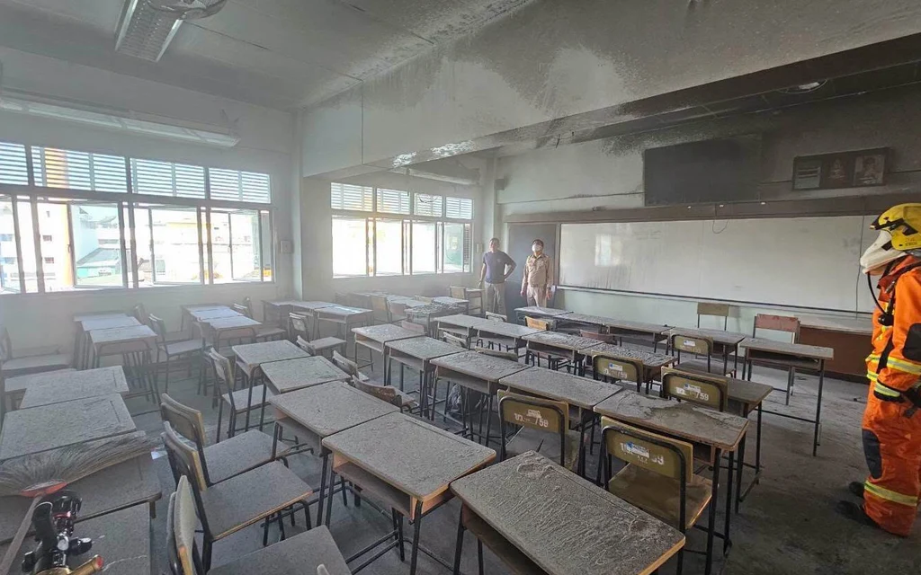 Firefighter inspects a smoke-damaged classroom filled with desks.