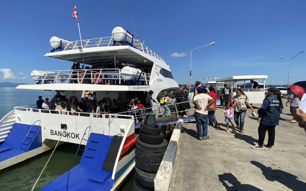 Tourists board a ferry at a pier in sunny weather.