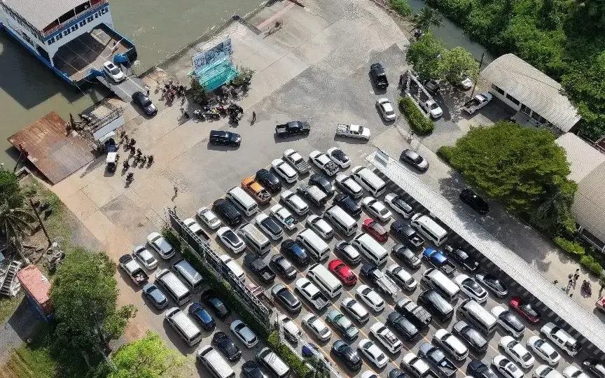 Aerial view of cars and people at a ferry terminal beside a river.