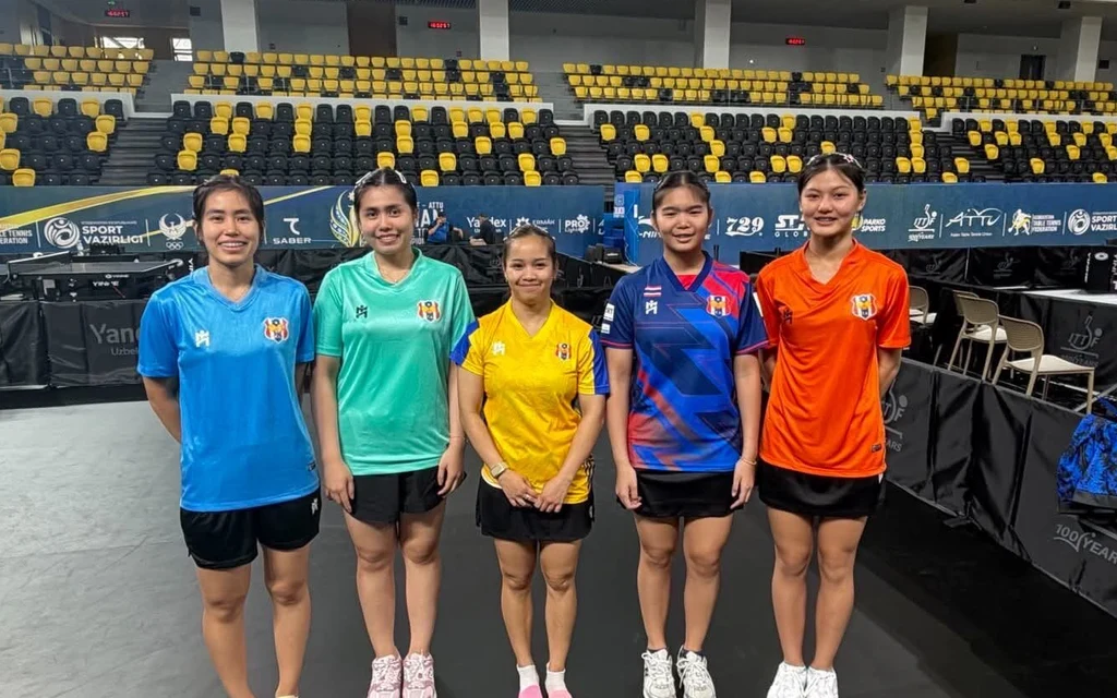 Five Thai table tennis players pose together inside an indoor sports arena.