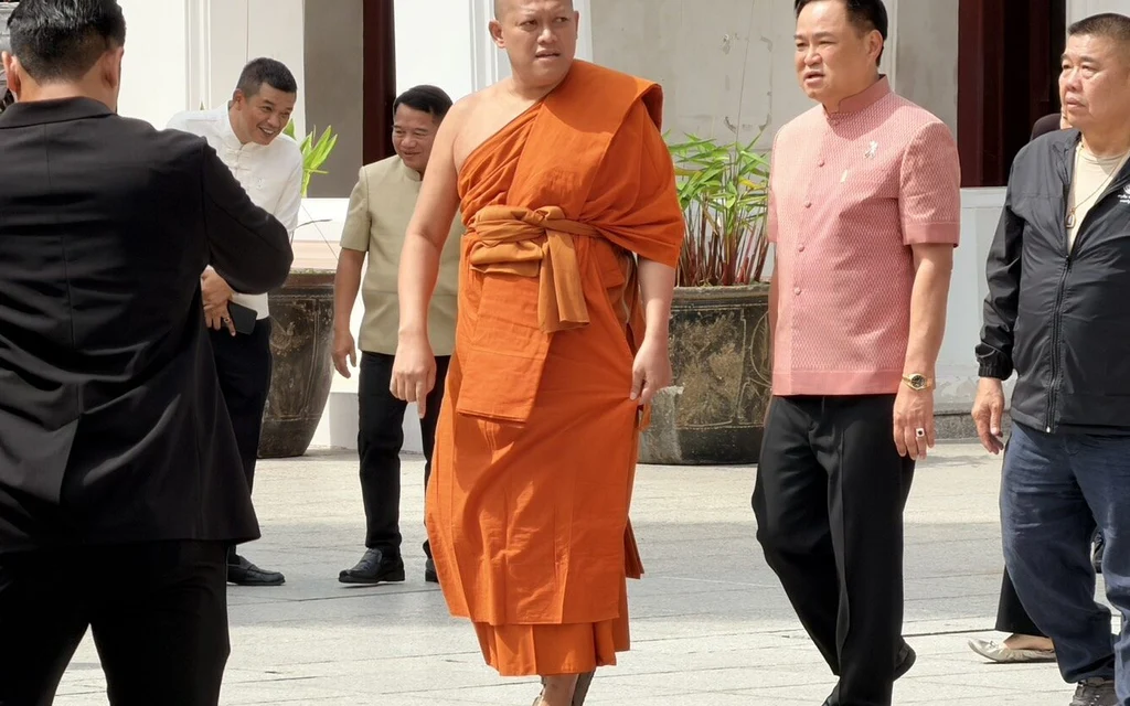 A Buddhist monk and officials walk outside a temple building.