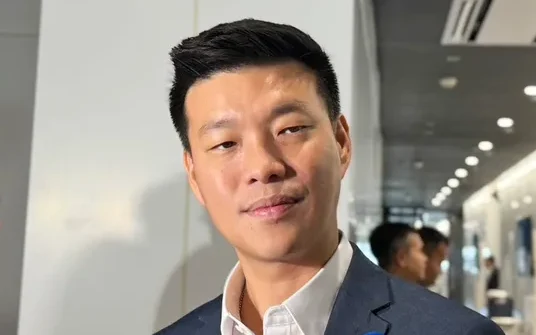 Man in a suit speaking to reporters in a hallway