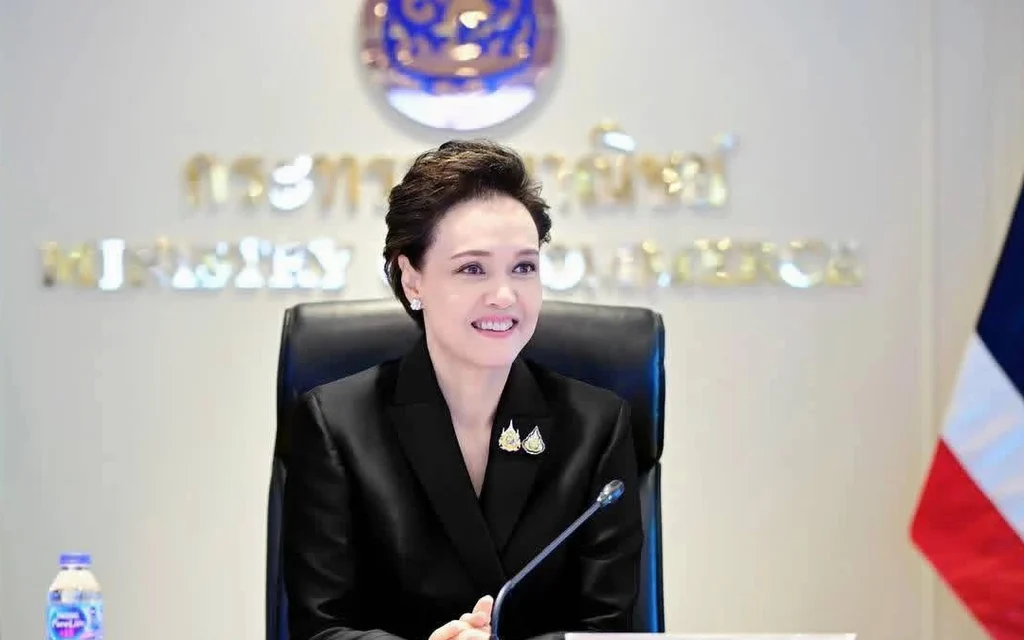 A woman chairs a meeting beside a Thai flag.