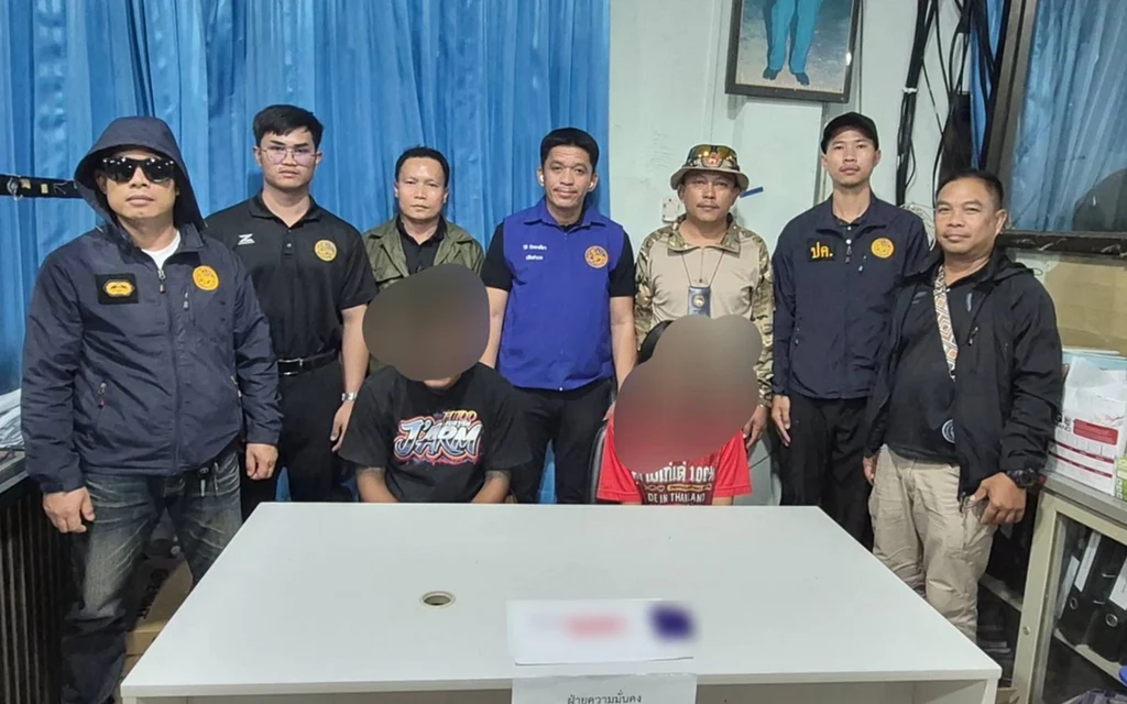 Officials pose with two blurred suspects and seized items on a table.