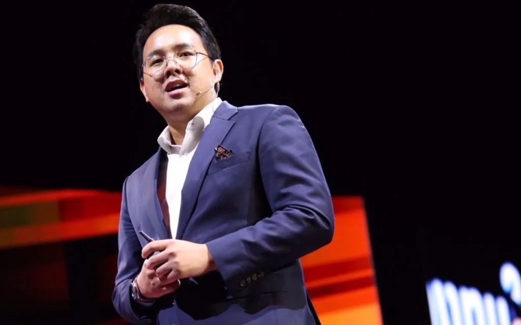A man in a suit speaks onstage at an event.