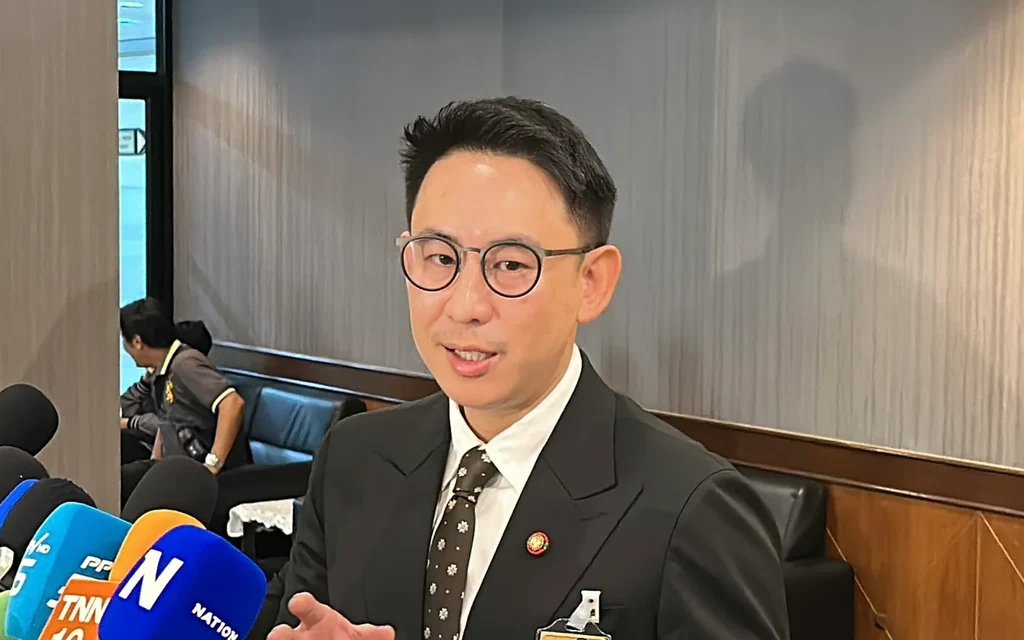 A suited man speaks to reporters surrounded by microphones.