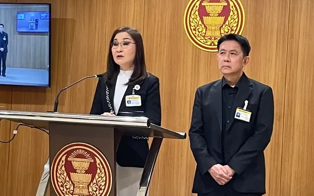 Two officials speak at a podium in a wood-paneled government room.