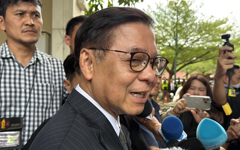 Thai official speaking to reporters with microphones in front of him.