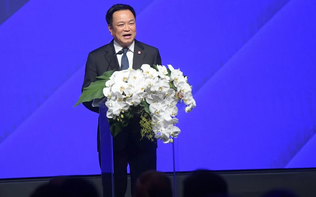 Anutin Charnvirakul speaking at a forum with a blue background.