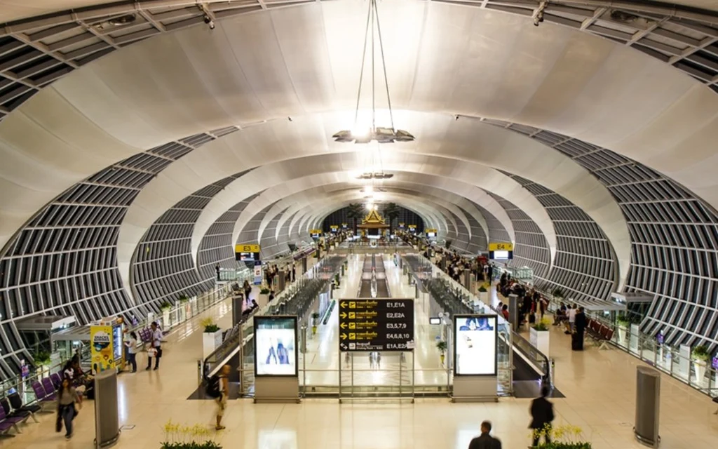 Wide interior view of a busy airport terminal with travelers and check-in counters.