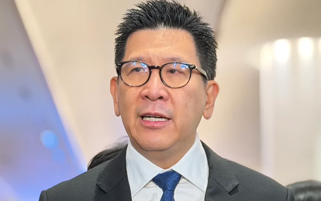 Finance minister speaking to reporters, wearing glasses and a dark suit.