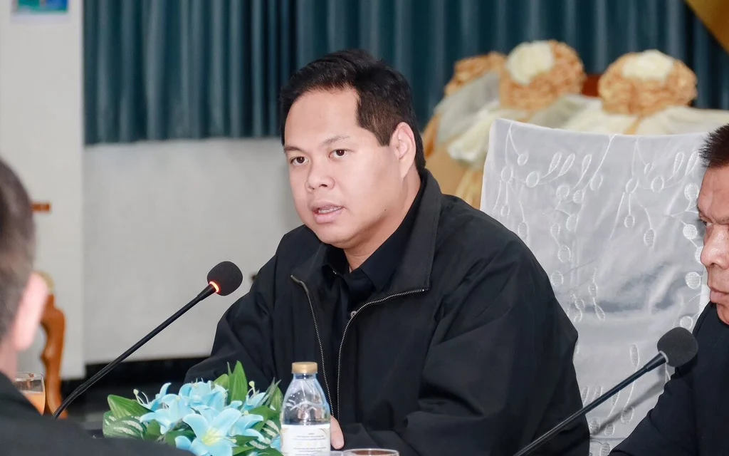 A man speaking at a meeting with microphones and water bottles.