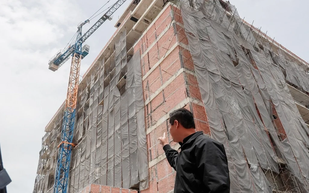A man pointing at a hospital building under construction with a crane.