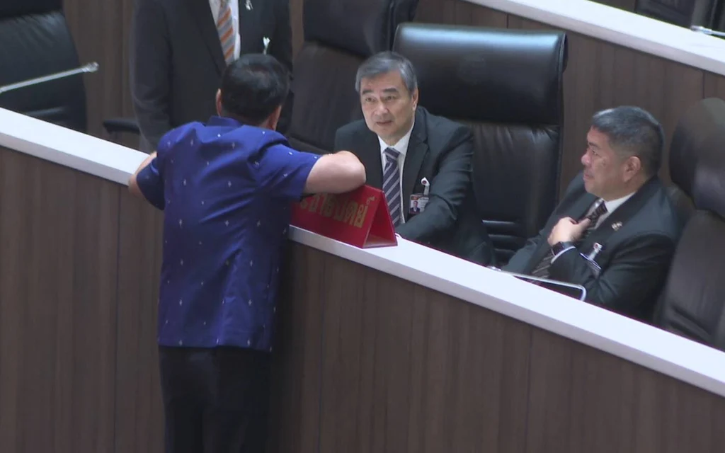 A man greets seated officials in a parliamentary chamber.