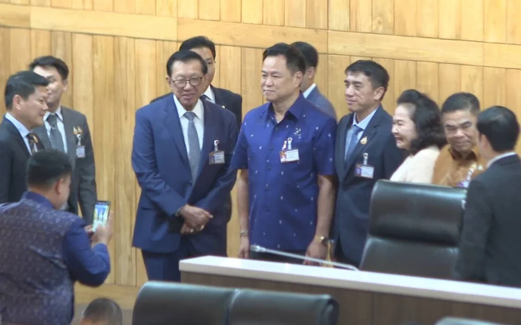 Politicians greet one another in a wooden-paneled parliamentary chamber.
