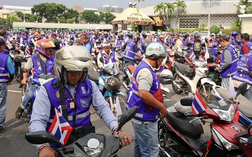 Motorcycle taxi drivers wearing blue vests gather with their motorcycles.