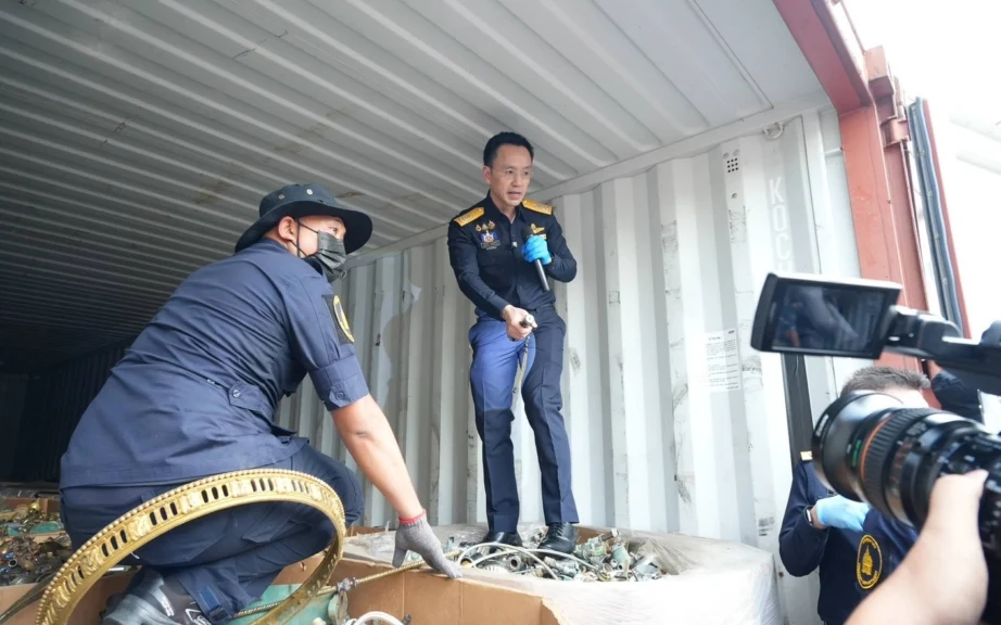 Customs officials inspect electronic waste inside a shipping container as media record them.