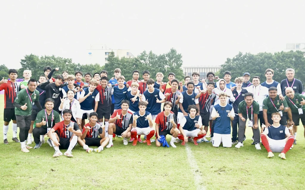 Football players and staff pose together on a grassy field.