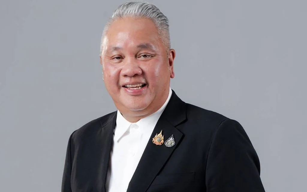 A man in a black suit poses against a plain gray background.