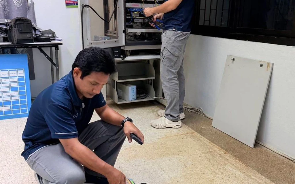 Two technicians work with tools and equipment inside a room.