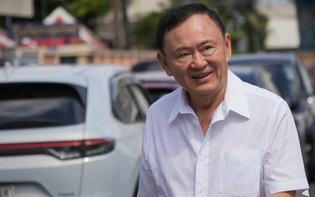 Thaksin Shinawatra smiling in a white shirt outdoors.