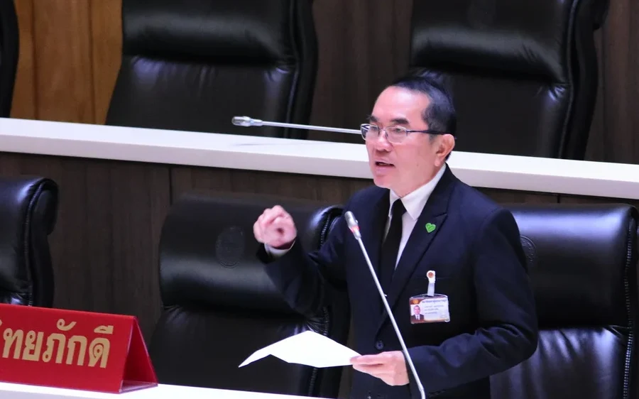 A suited politician speaks and gestures at a parliamentary desk.