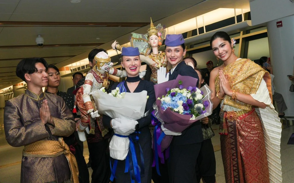 Performers in traditional Thai costumes pose with flowers in a hallway.