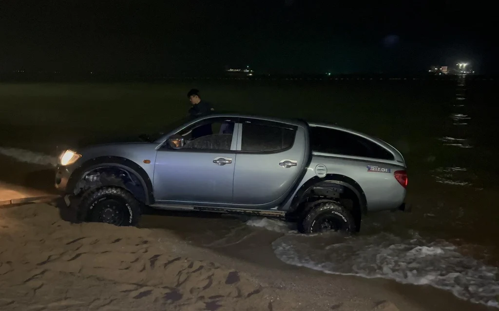 A pickup truck is stuck in shallow water on a dark beach.