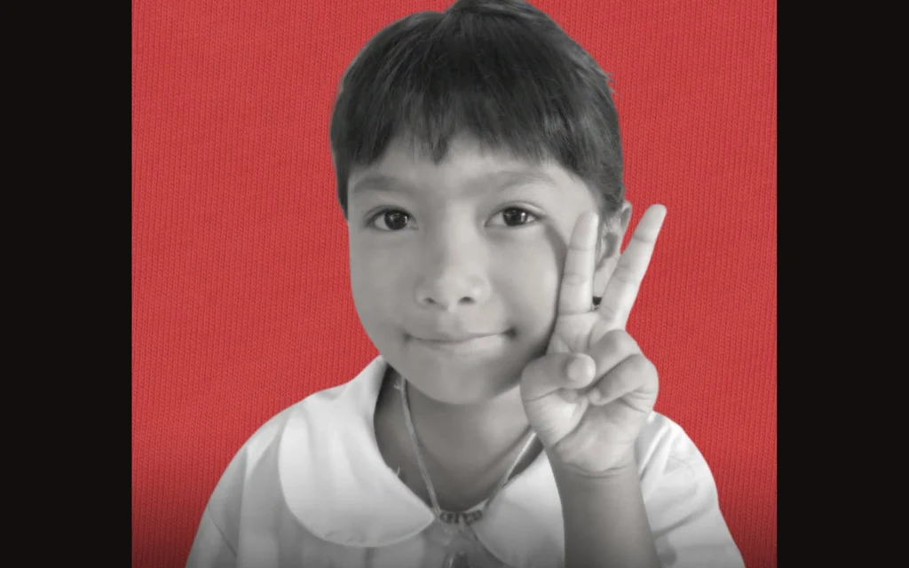 A black and white portrait of a young girl making a peace sign.