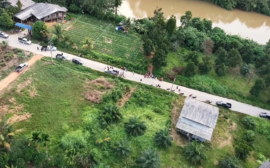 Aerial view of a rural road, fields, houses, vehicles, and a river.