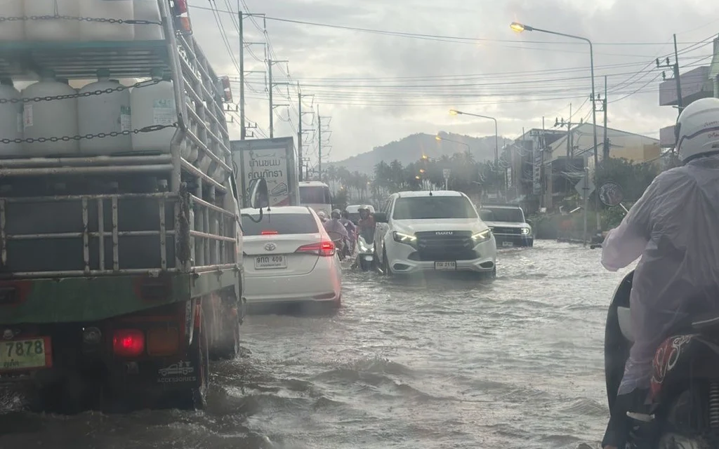 Vehicles and motorcyclist navigate a flooded street in heavy rain.
