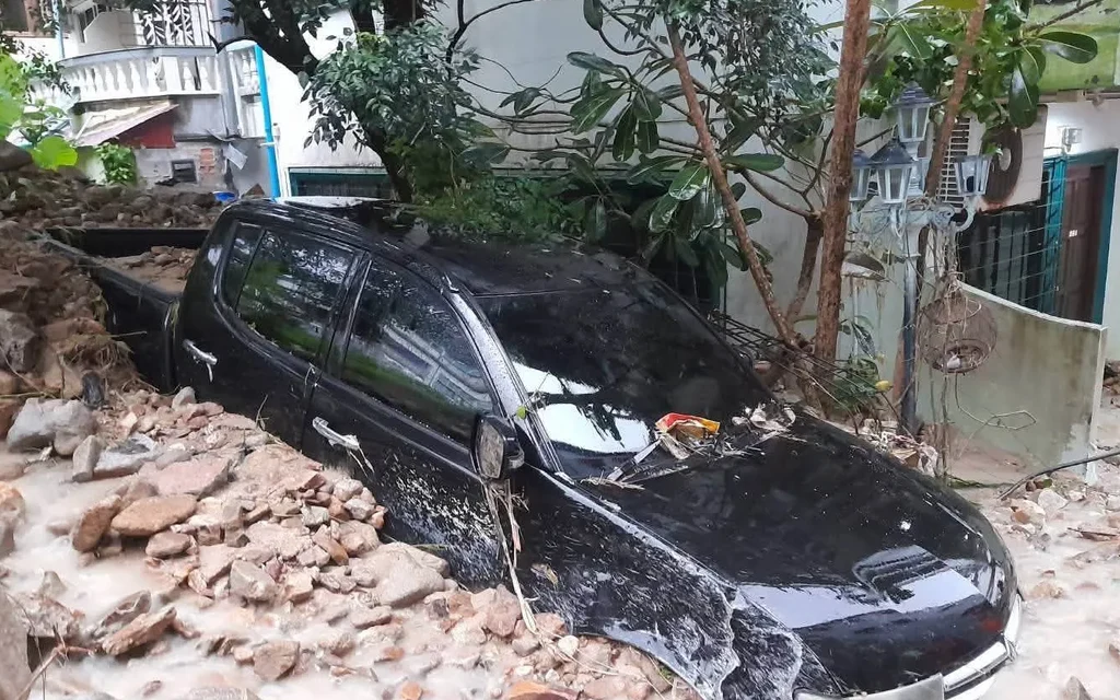 Black car partly submerged in muddy floodwater and surrounded by rubble.
