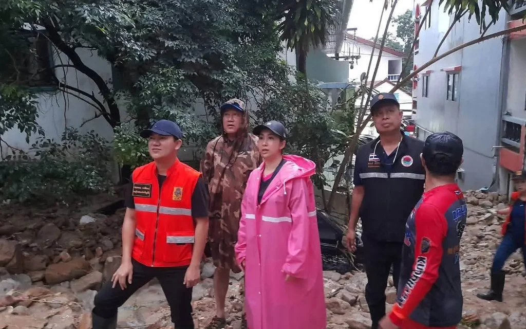 Officials and residents walk through a rain-damaged area amid scattered rocks.