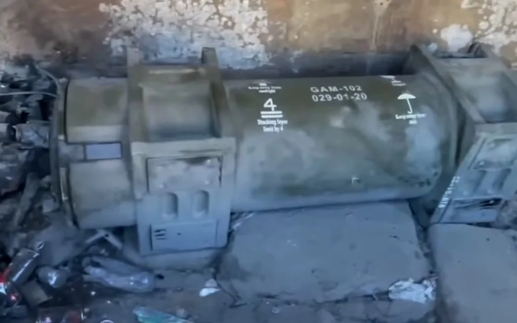 A damaged military container lies amid rubble inside a ruined building.
