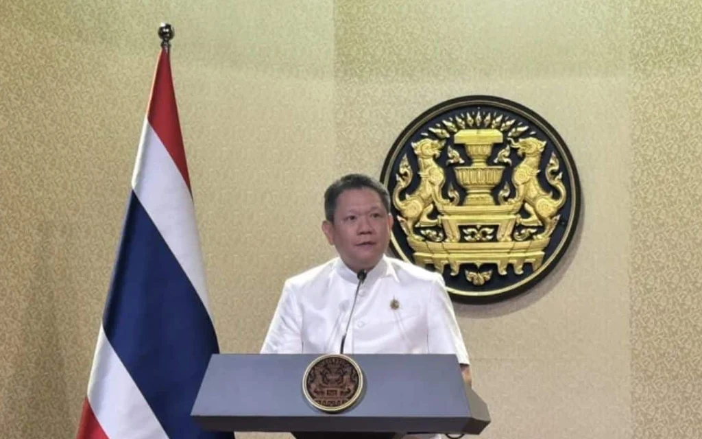Thai finance official speaking at a podium beside the national flag