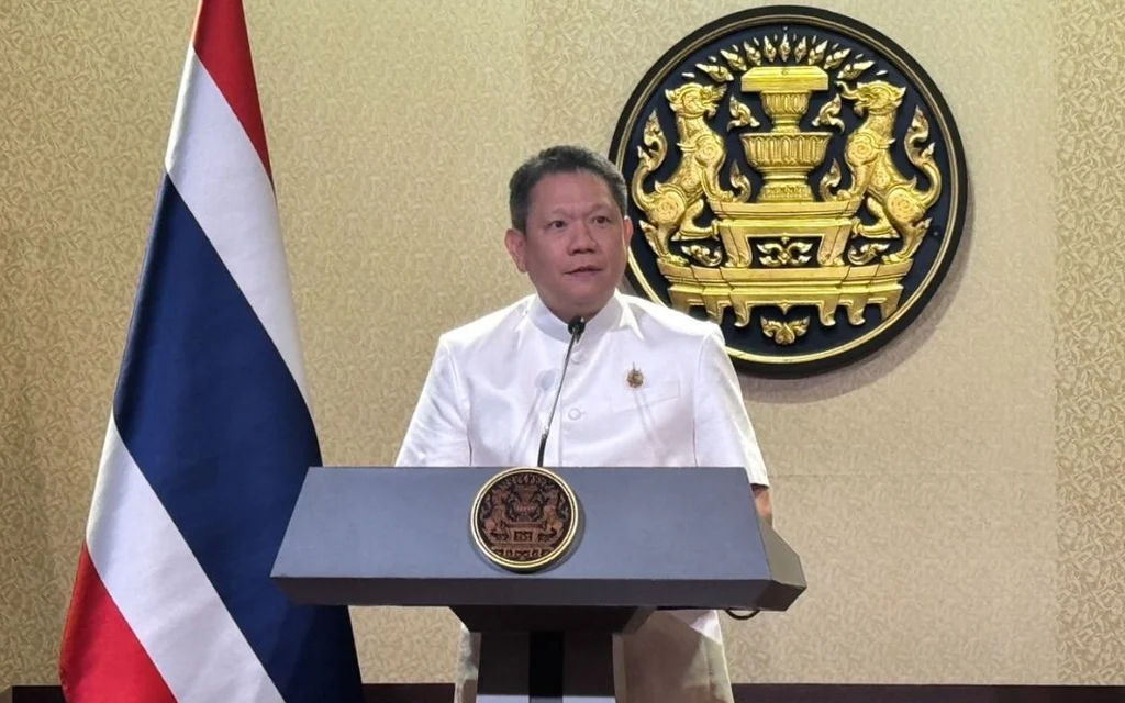 Thai finance official speaks at a podium beside the national flag.