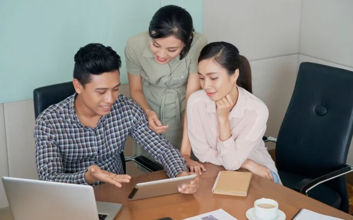 Three adults review materials around a laptop at a meeting table.