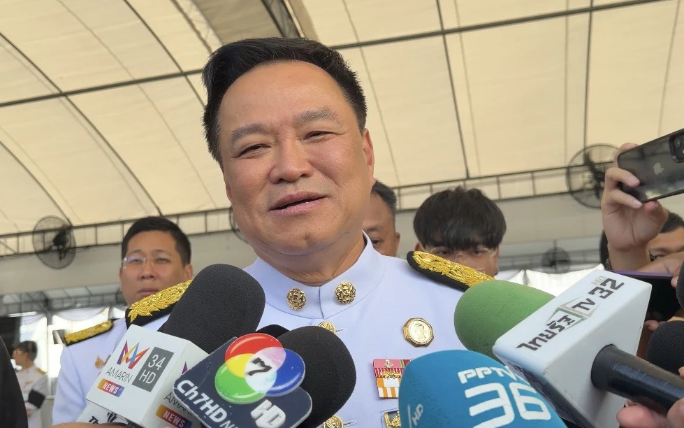 Thai official speaks to reporters surrounded by journalists and microphones.