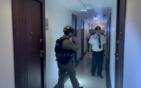 Police officer and hotel staff member stand in a condominium hallway.