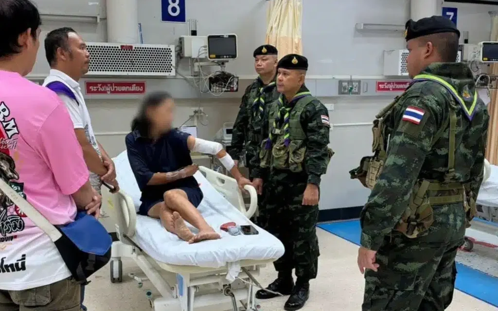 Wounded woman speaks with Thai soldiers and bystanders in a hospital ward.